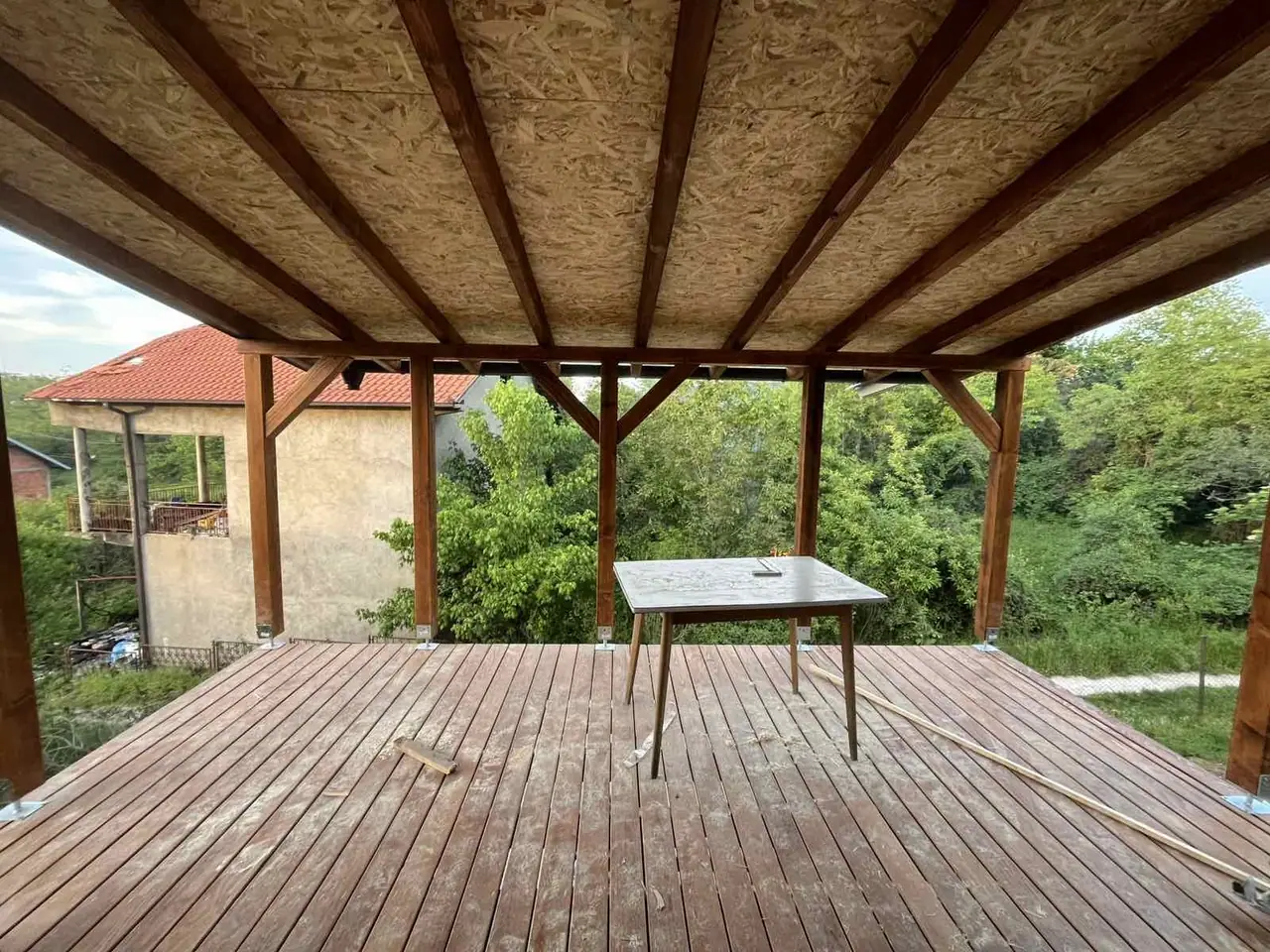 Natkrivena terasa sa drvenim podom i stolom, pogled ka zelenilu